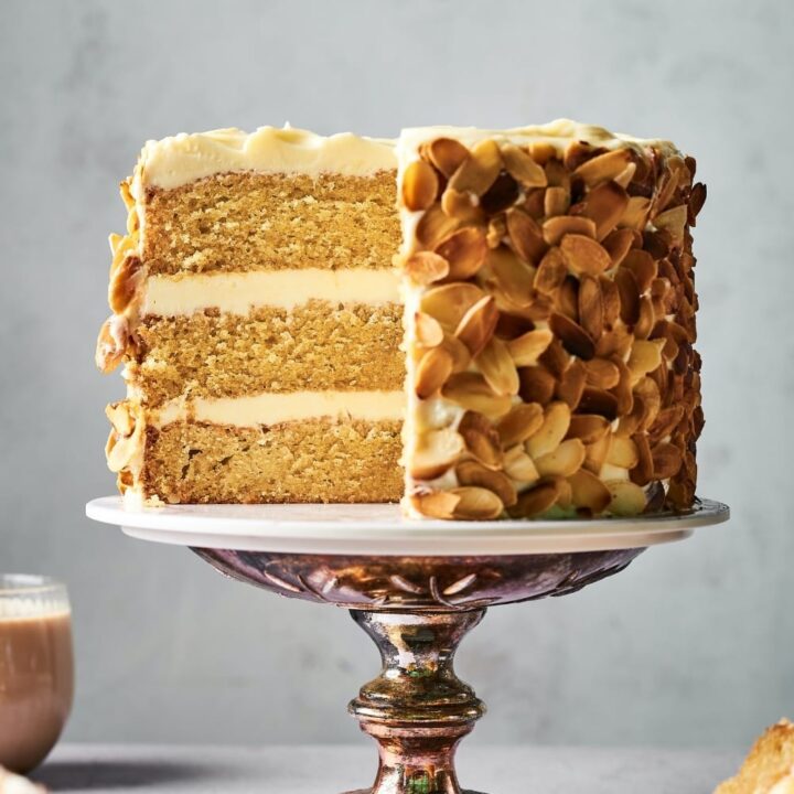 A burnt almond cake on a cake platter. The front left side of the cake is gone, showing the inside of the cake.