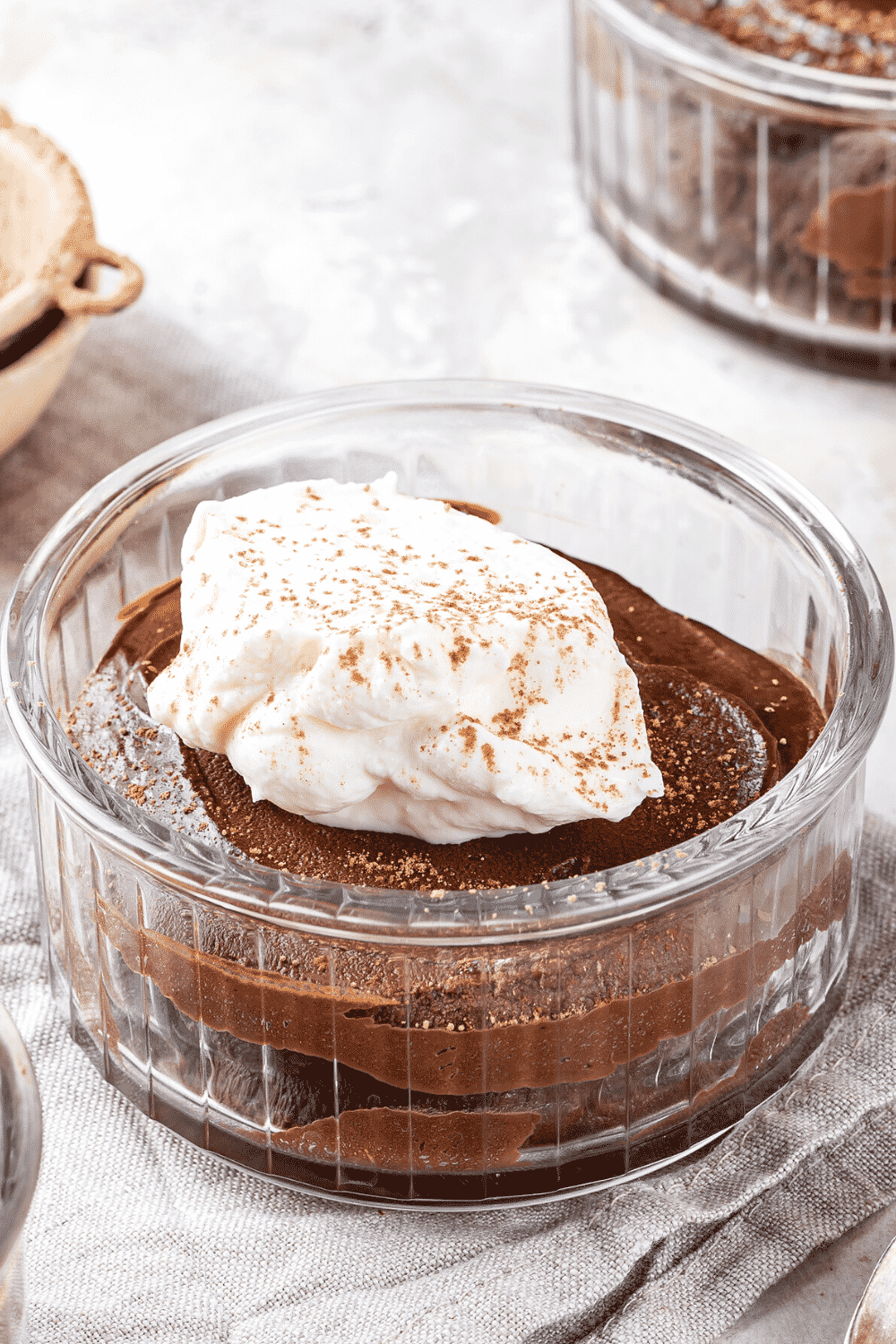 A small glass bowl filled with chocolate mousse. A dollop of whipped cream is on top of the mouse.