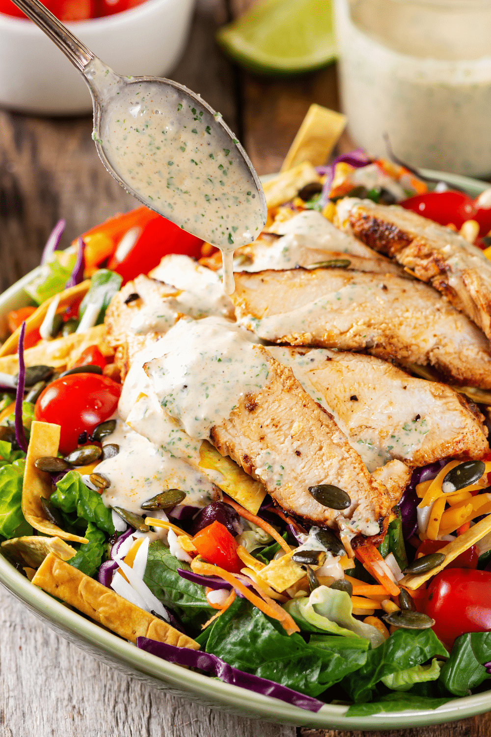 A white bowl filled with spicy southwest salad. A spoon is drizzling creamy salsa dressing over the chicken that is on top of the salad.