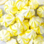 A bunch of lemon meringue cookies on top of one another on a piece of parchment paper.