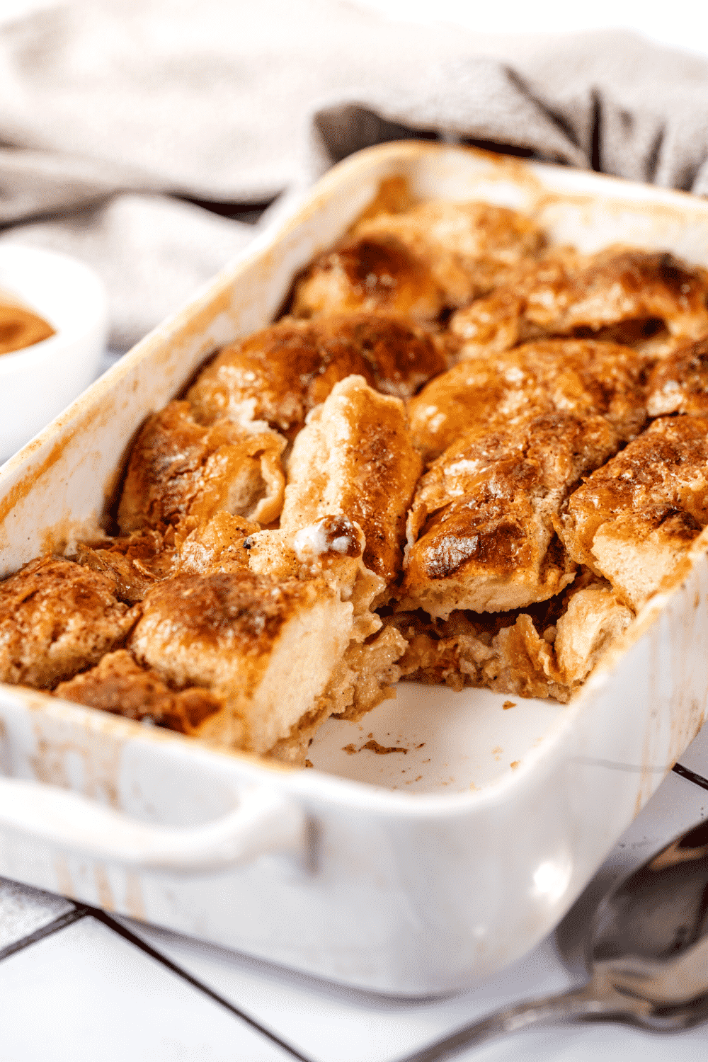 White casserole dish with bread pudding in it. There is a chunk of bread pudding taken out of the front of the casserole dish.