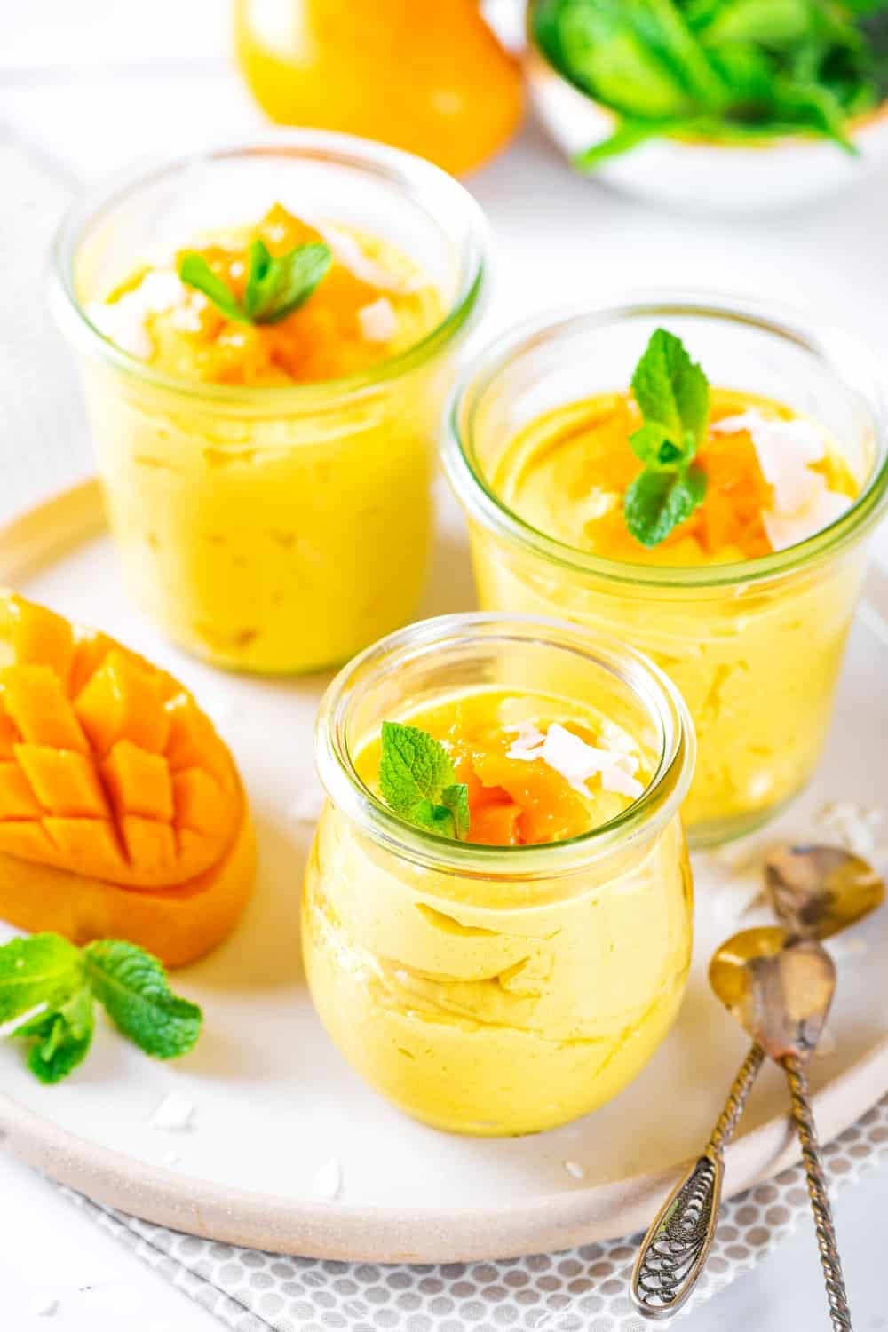 3 glass cups of mango mousse on a white plate.