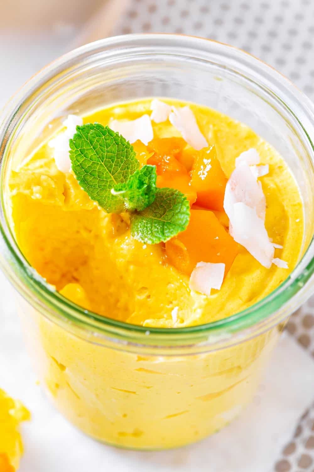 Glass cup filled with mango mousse. Part of the mango mousse on the front left of the cup is missing.