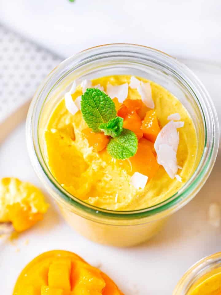 An overhead view of a glass cup of mango mousse on a white plate.