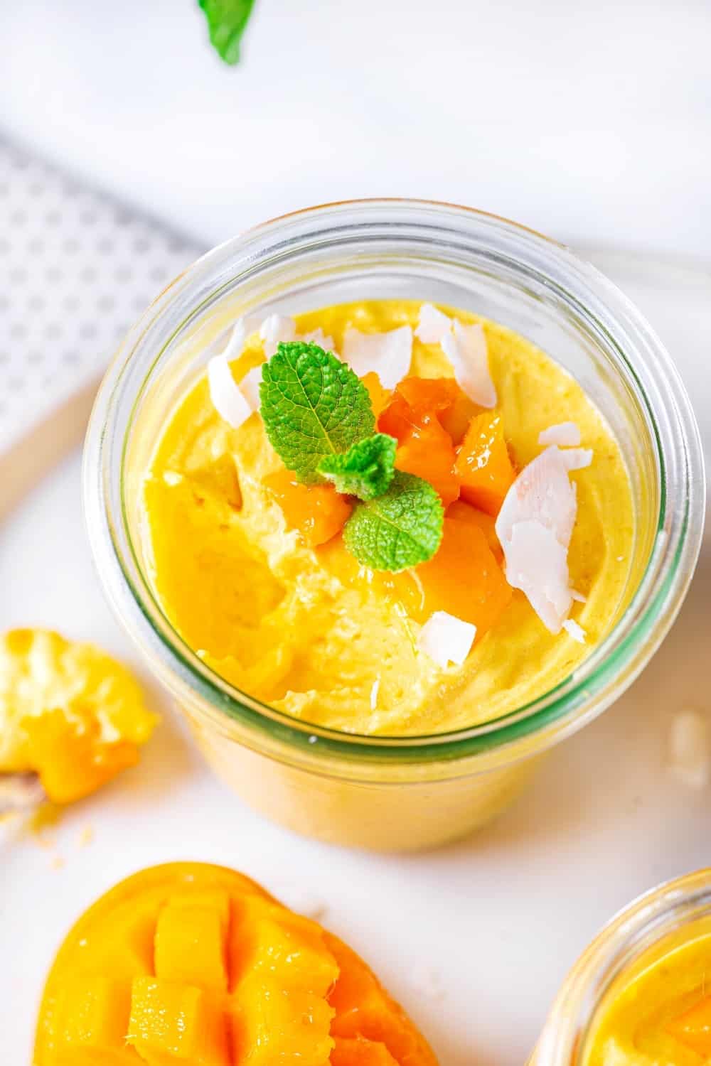 An overhead view of a glass cup of mango mousse on a white plate.