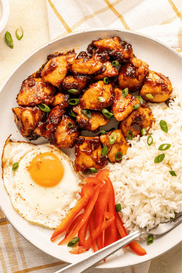 A white plate with chicken tocino a fried egg sliced red bell peppers and white rice on it.