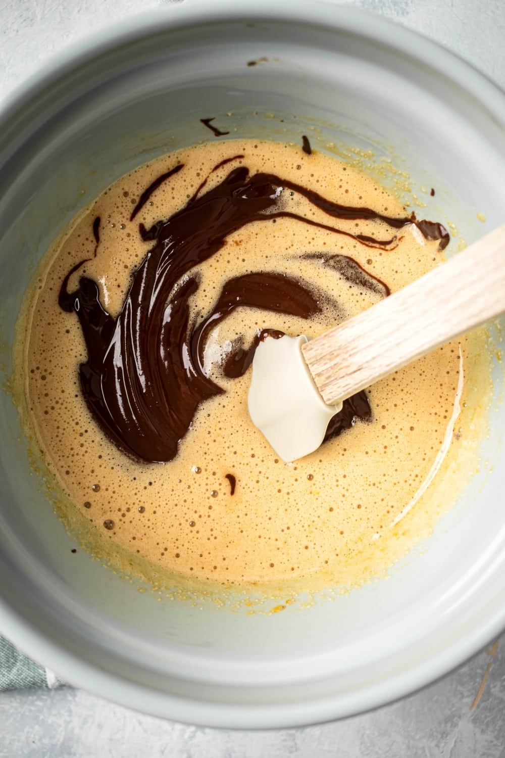 A bowl with white brownie batter ingredients and melted chocolate in it.