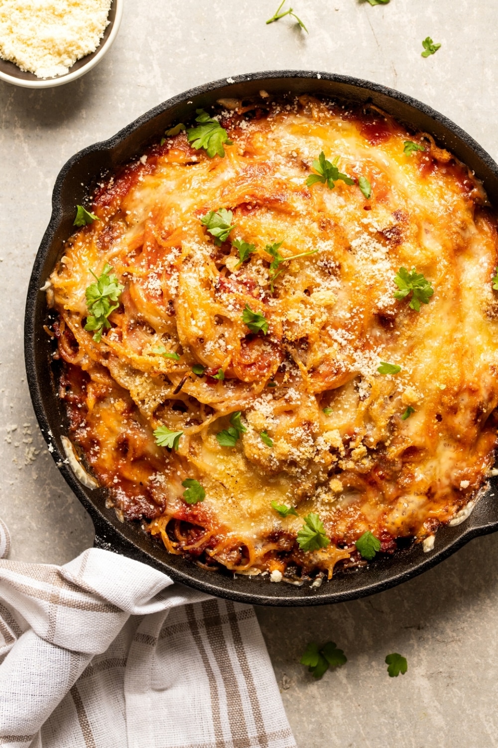 A cast-iron skillet filled with fried spaghetti. Hey white plaid napkin is on the handle of the skillet and the skillet is on a gray counter.