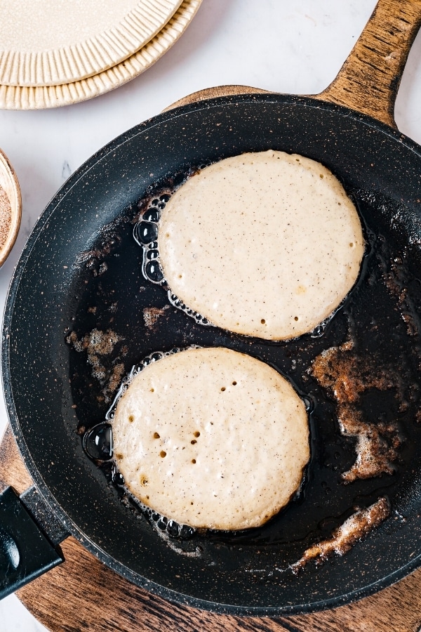 Two churro pancakes cooking on a skillet.