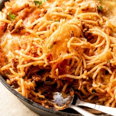 Fried spaghetti in a cast-iron skillet. Some of the noodles are on top of the melted cheese and there was a spoon and fork in place of the noodles at the front of the skillet.