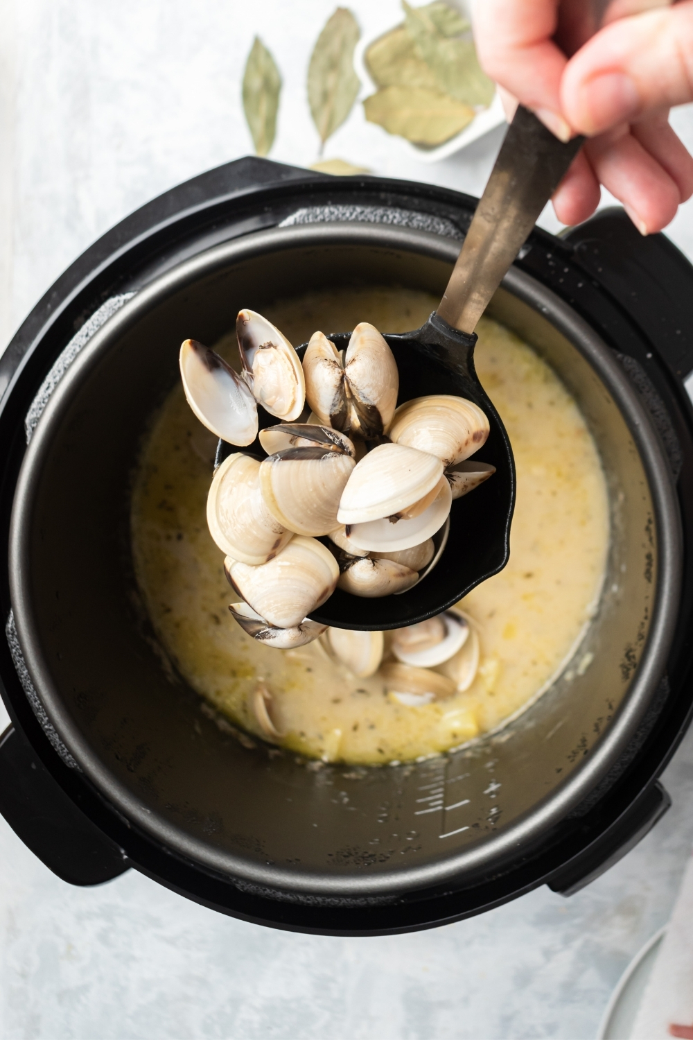 A hand holding a ladle over an instant pot filled with clam chowder.