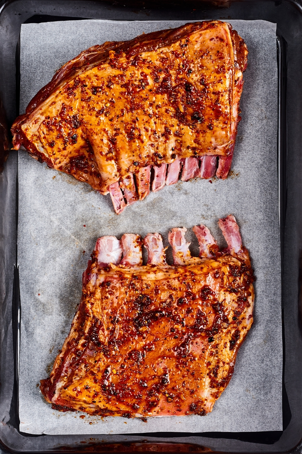 A baking dish lined with parchment paper with two marinated lamb breast on it.