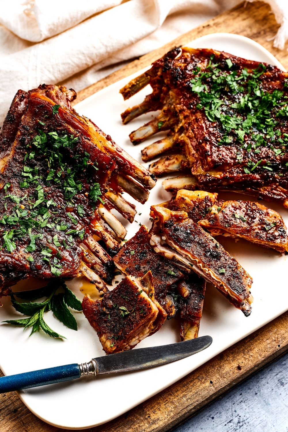 Part of a rectangular white plate with two lamb breasts and slices of lamb rest in front of them with a knife in front of that.