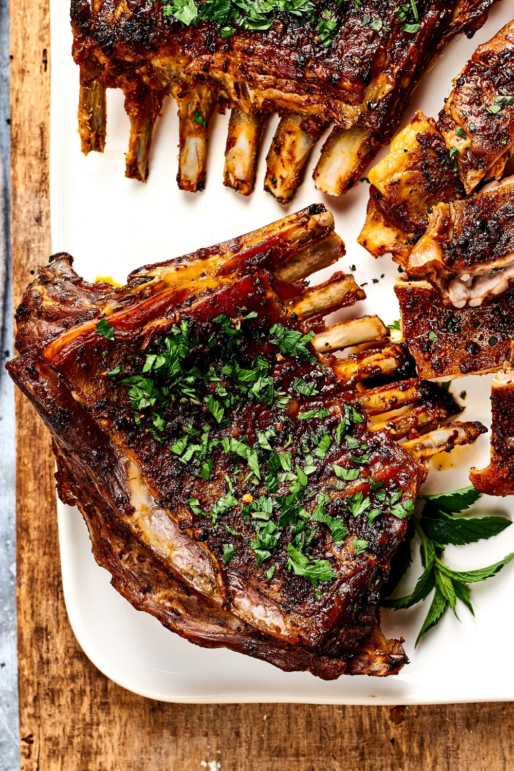 Part of a white plate with the lamb breast on it and parts of other lamb breasts. The plate is on a wooden counter.