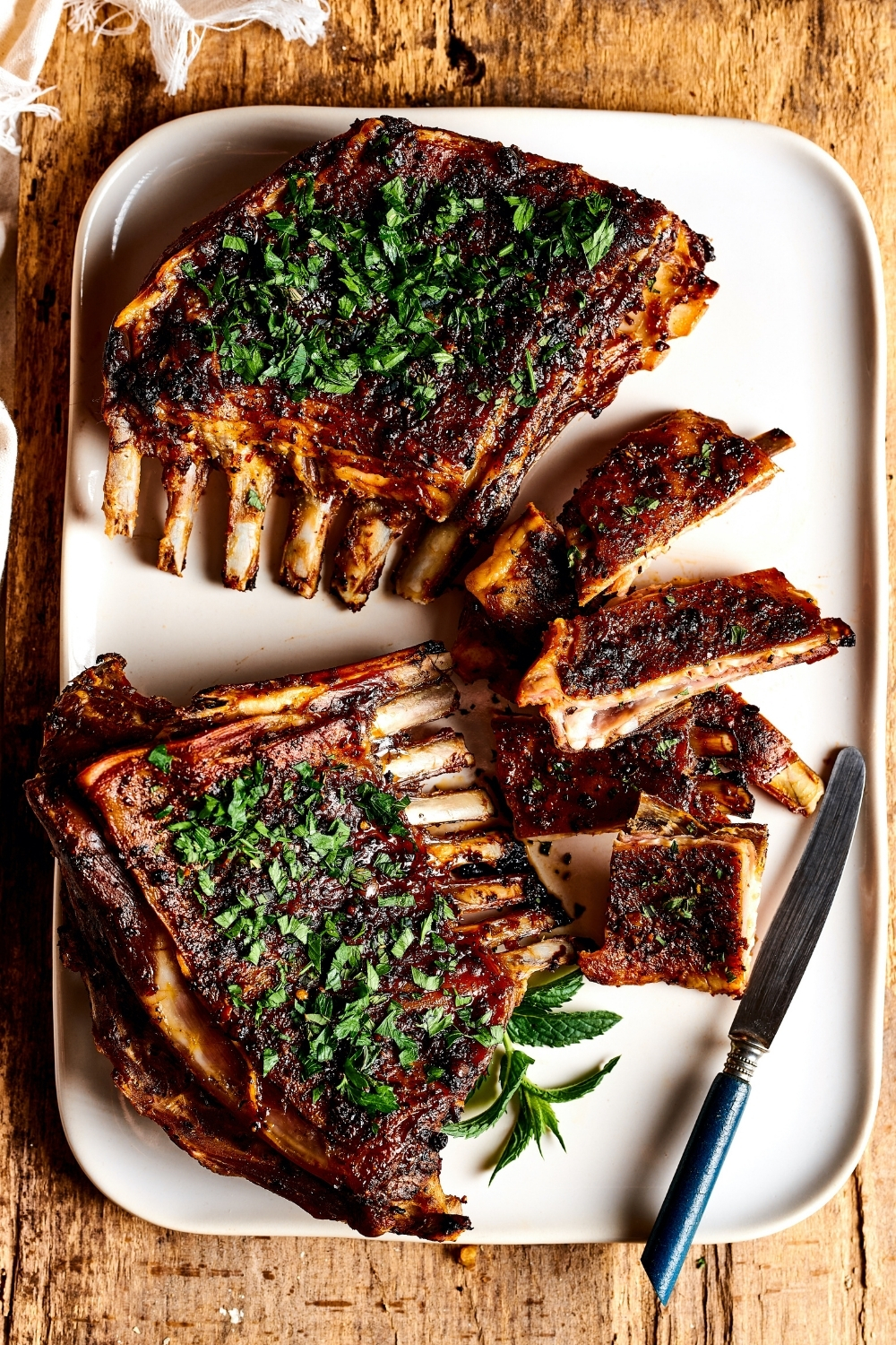 A rectangular White plate with two lamb breasts on it. To the right of the lamb breasts are a few sliced pieces of lamb breast with a knife next to them.