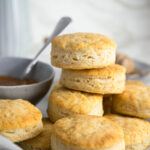A bunch of biscuits on top of one another on a piece of parchment. To the left of the biscuits on the plate as part of a bowl of gravy.