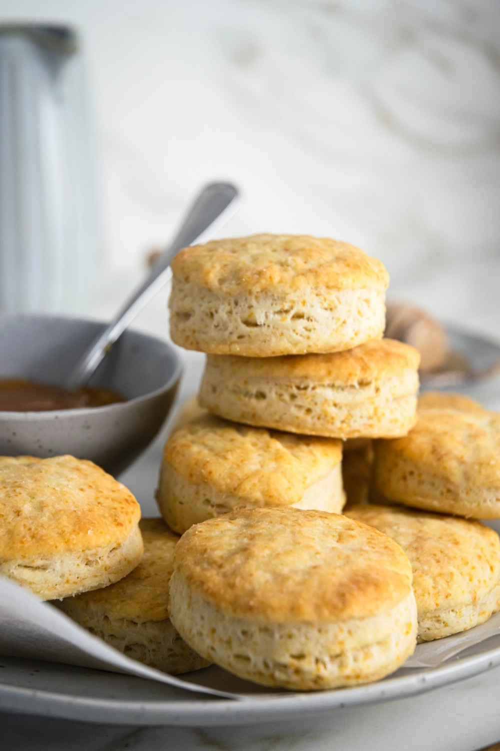 A bunch of biscuits on top of one another on a piece of parchment. To the left of the biscuits on the plate as part of a bowl of gravy.