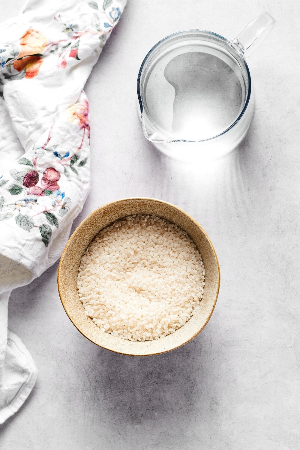 A small bowl of sushi rice on a white counter with a pitcher of water behind it.