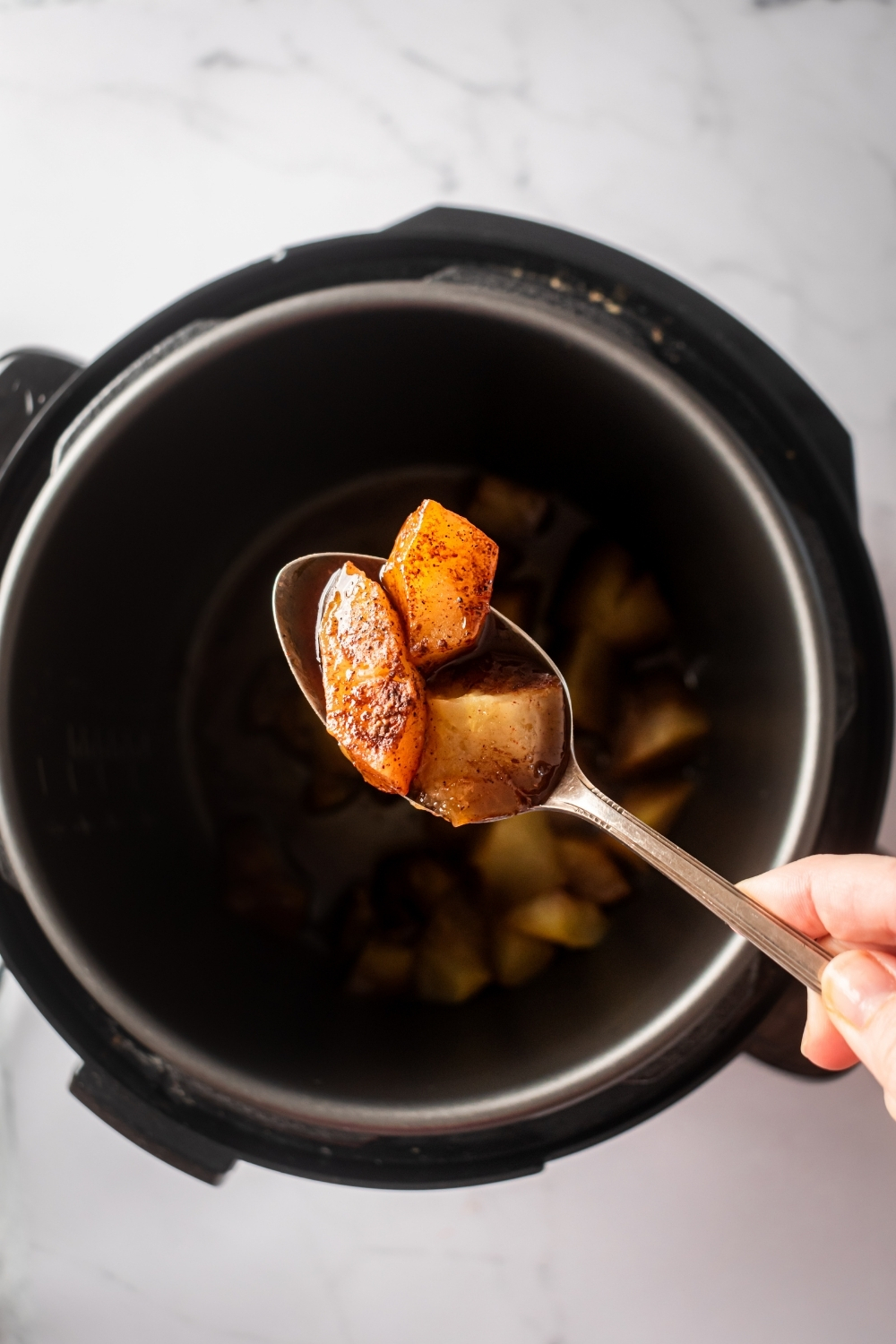 A spoon with two slices of apple on it being held over an instant pot filled with apple butter.