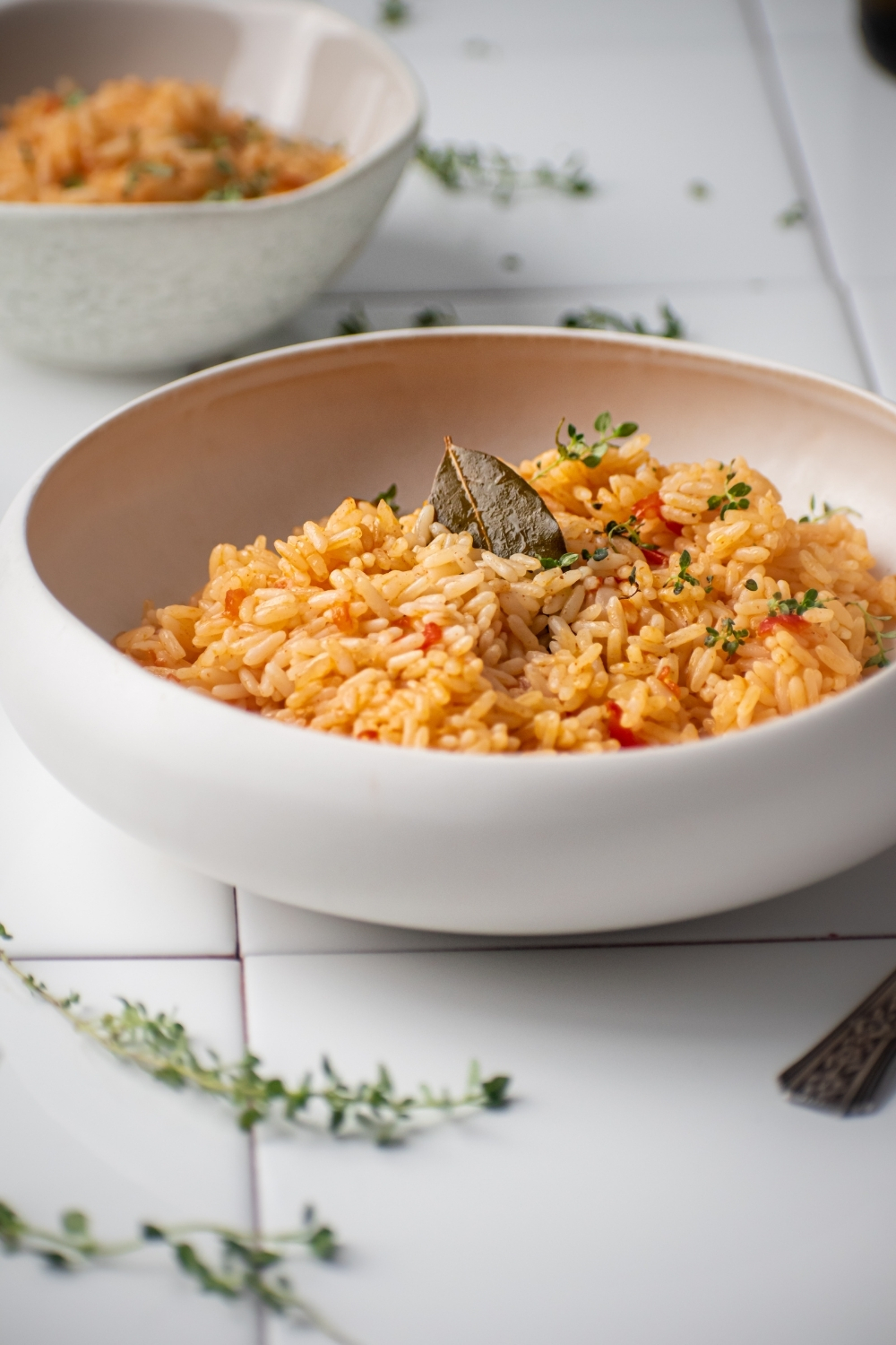 A white bowl filled with Spanish rice. The ball is on white tile and behind it is part of a smaller white bowl with Spanish rice in it.