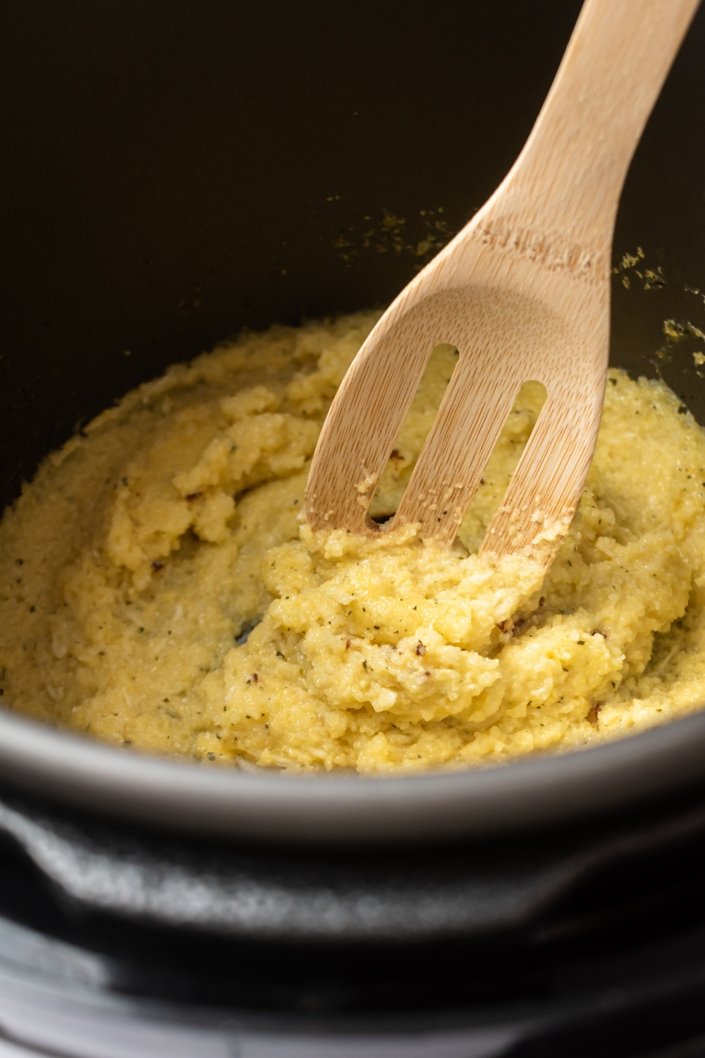 Polenta cooking in an instant pot with a wooden spoon submerged in the polenta.