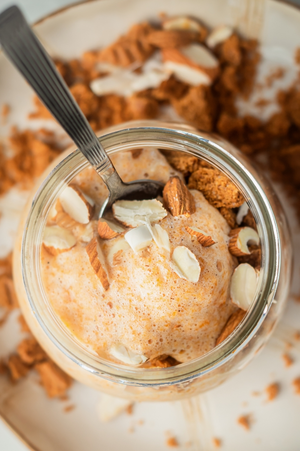 A white plate with a glass jar on top of it filled with pumpkin mousse. There is a spoon submerged in the top of the pumpkin mousse.