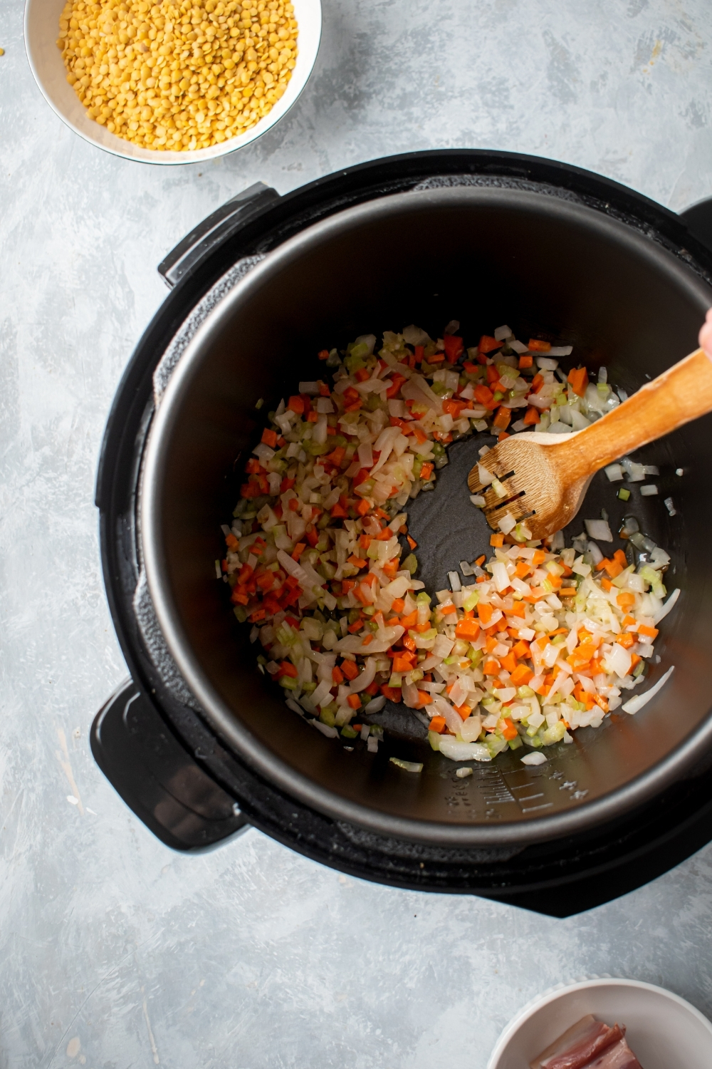 An instant pot filled with chopped carrots onions and celery. The instant pot is on a gray counter and behind it as part of a small white bowl filled with yellow split peas.