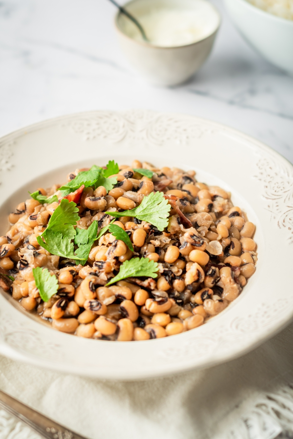 A white bowl filled with black-eyed peas on a white tablecloth.