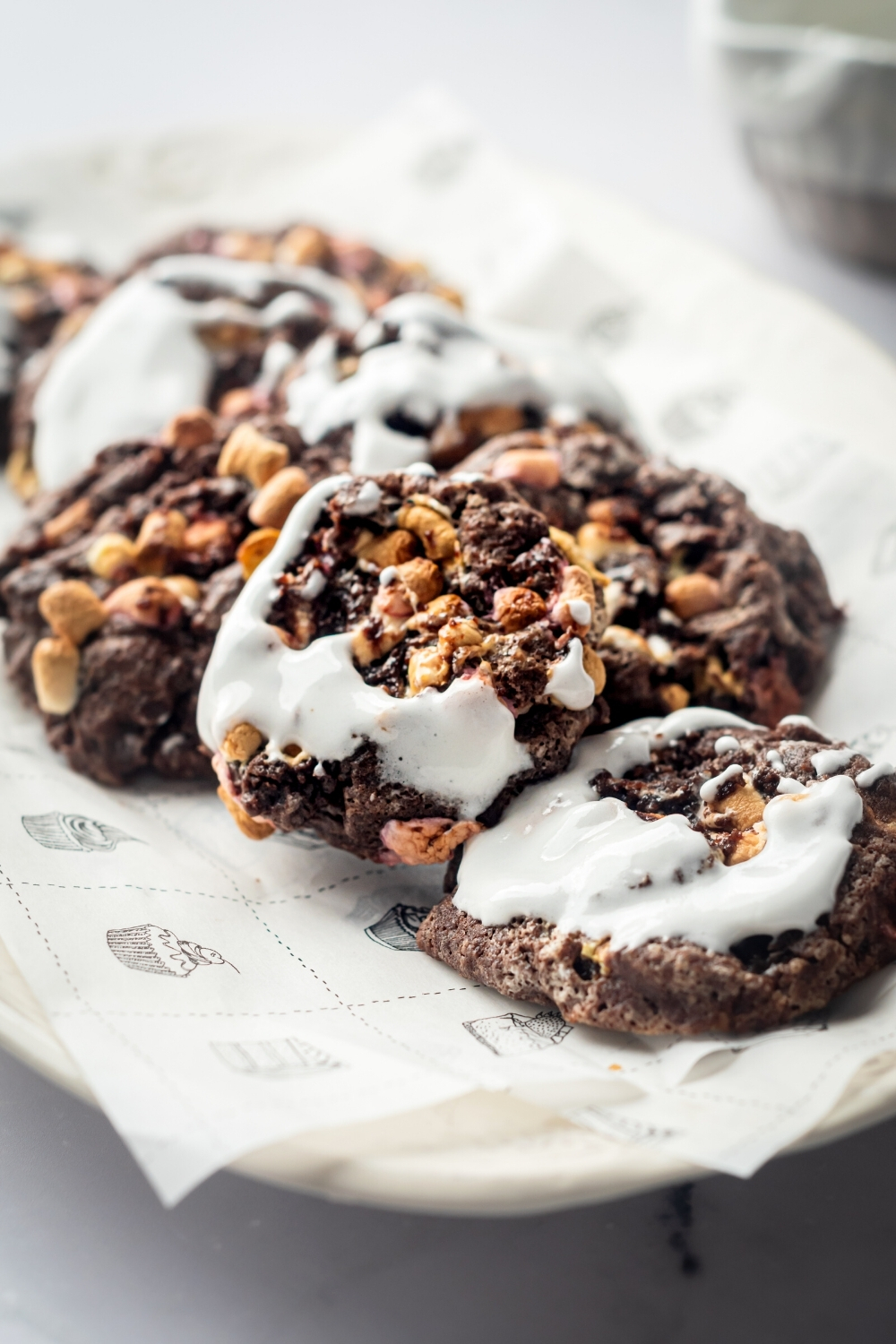 A bunch of chocolate marshmallow cookies covered in fluff on a piece of parchment paper on a white plate.