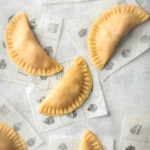 A few empanadas on individual square sheets of parchment paper all on a gray counter.