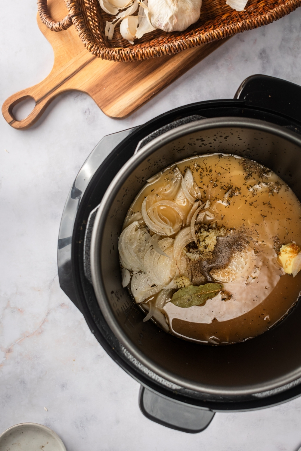 And instant pot on a white counter filled with French onion soup ingredients.