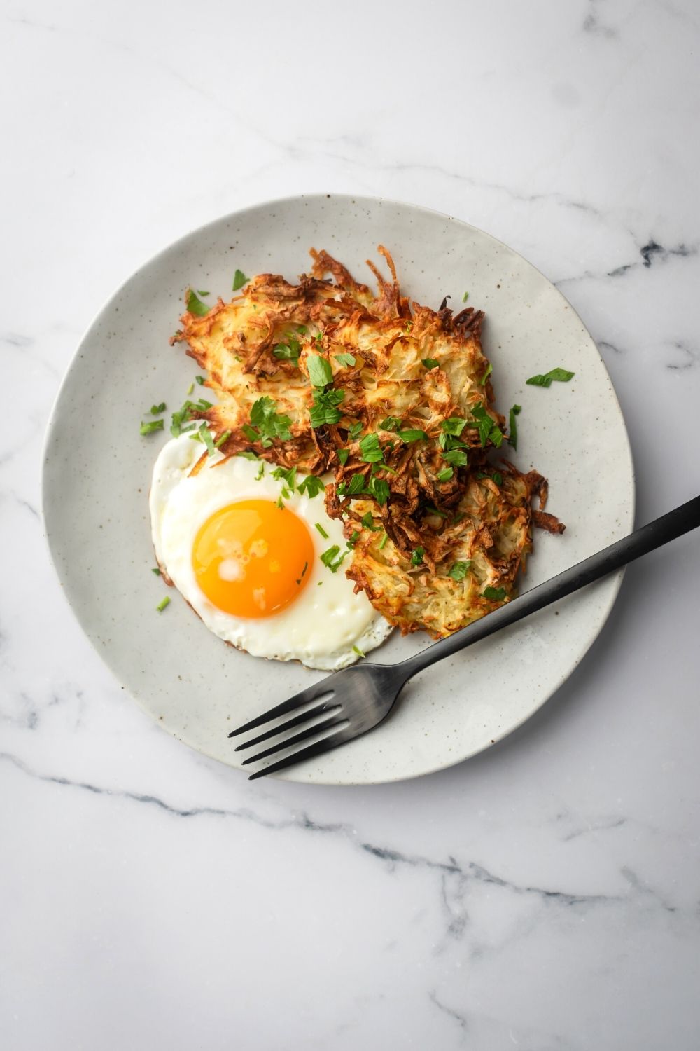 A gray plate on a gray counter with three hash browns for fried egg and a fork on it.