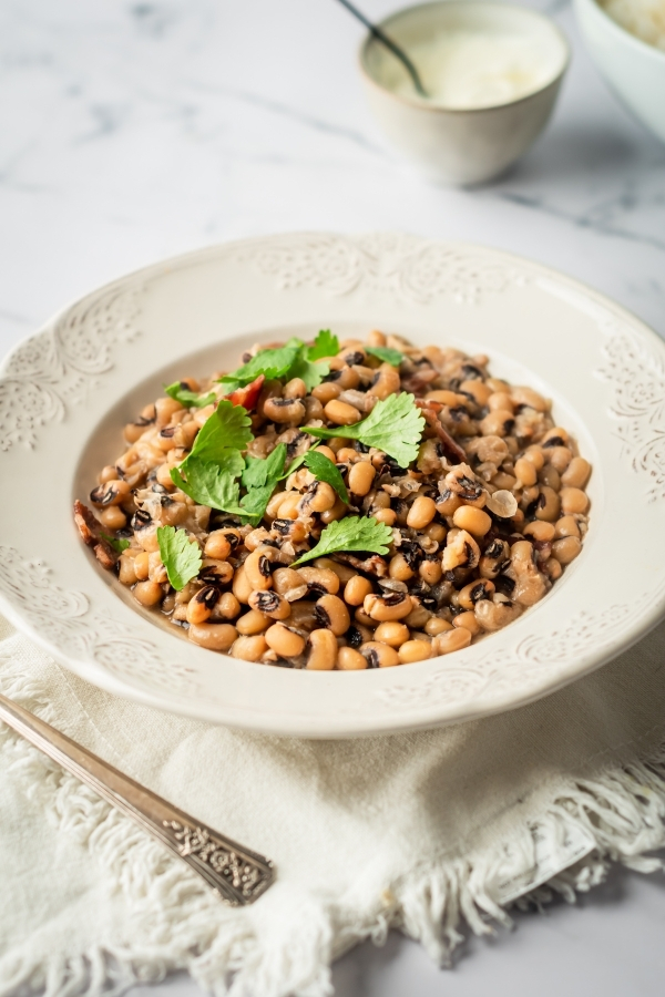 A white bowl filled with black eyed peas on top of a white tablecloth that is on a white counter.