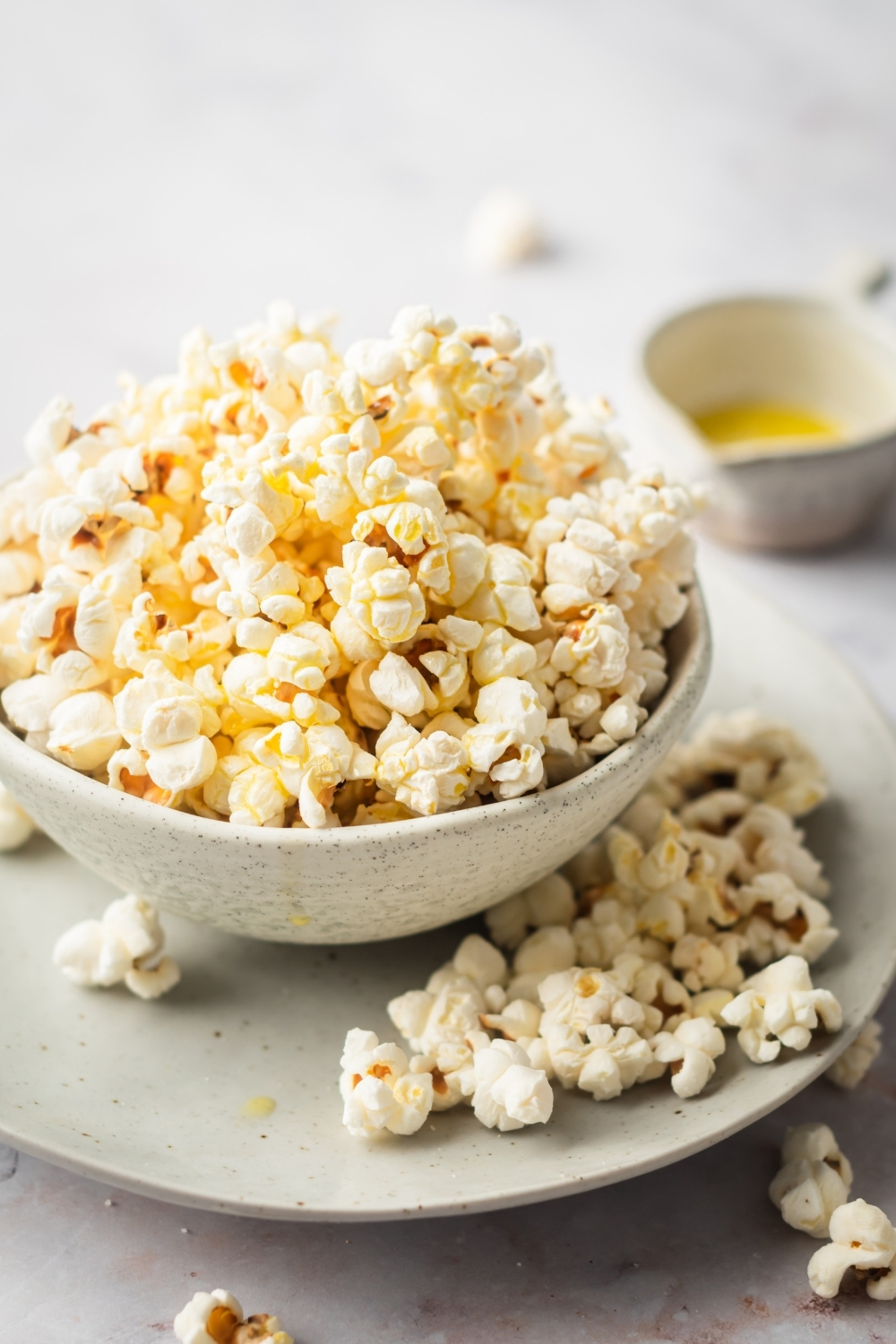 And a bowl of popcorn on a plate with some more popcorn on it on the white counter. Behind the plate is a small cup of some melted butter.