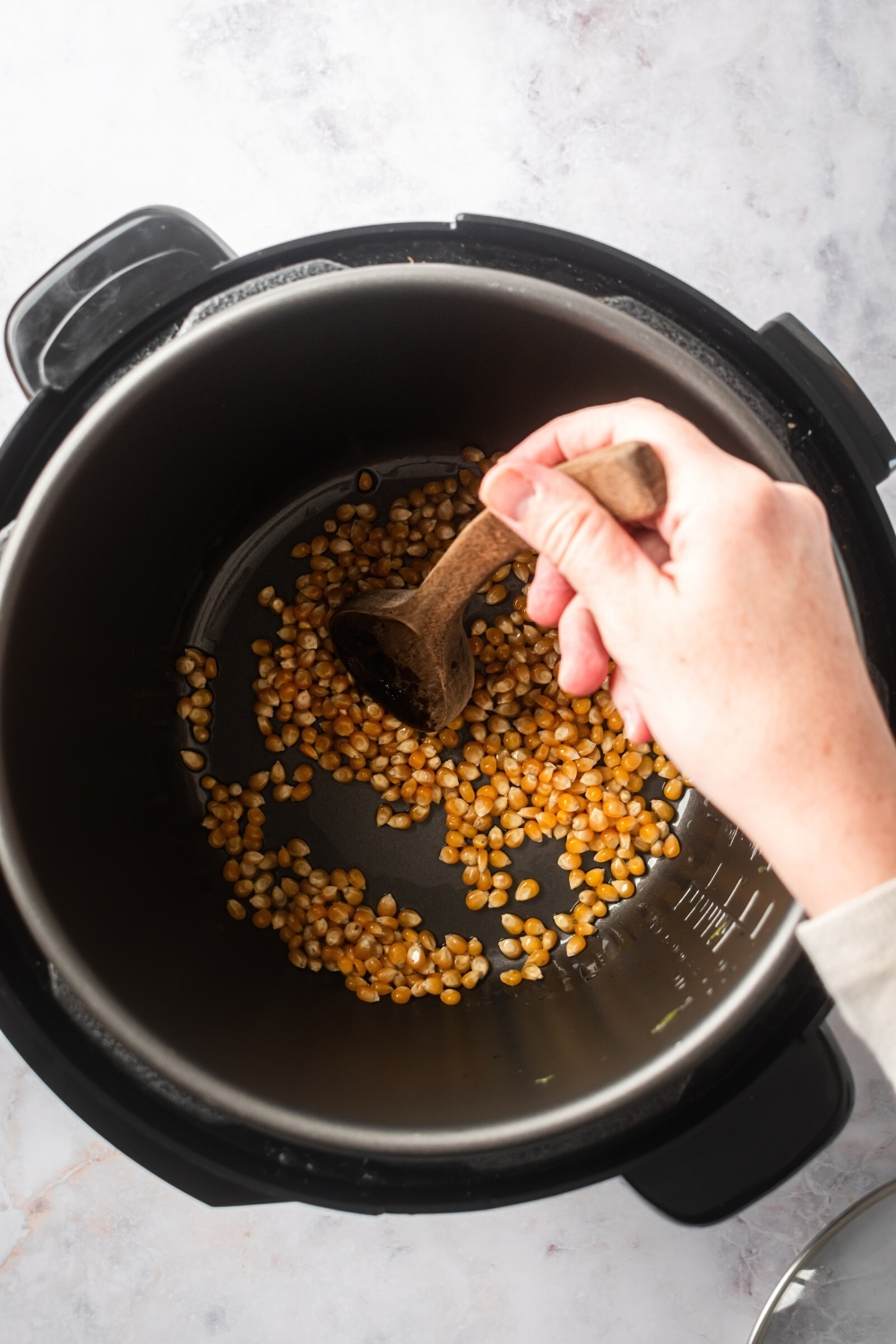 A hand stirring popcorn kernels around in an instant pot.
