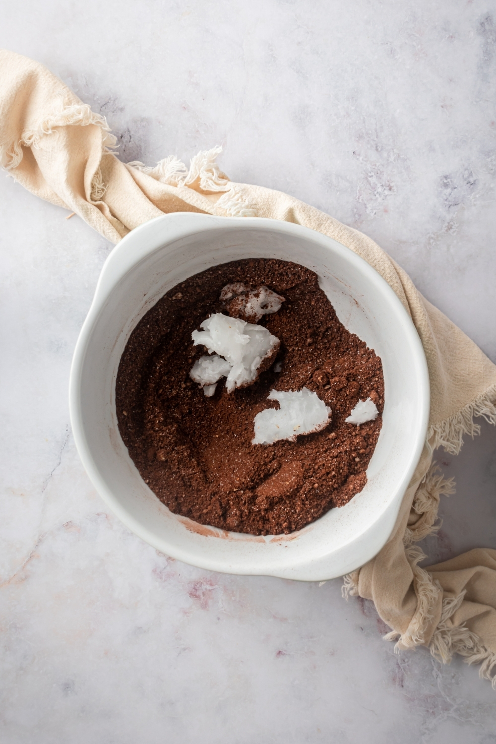 A white bowl filled with chocolate almond flour crust ingredients with coconut oil in it.