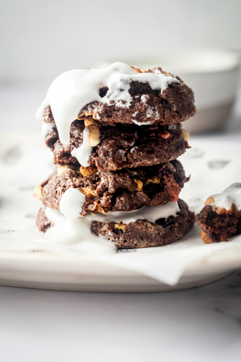 For chocolate marshmallow cookies stacked on top of one another on a piece of parchment paper on a white plate. There is fluff on the top cookie dripping down the front side of it.