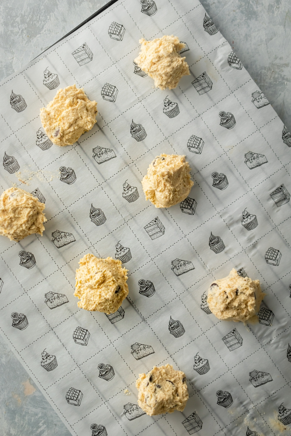 A tray lined with parchment paper with seven balls of cookie dough on it.