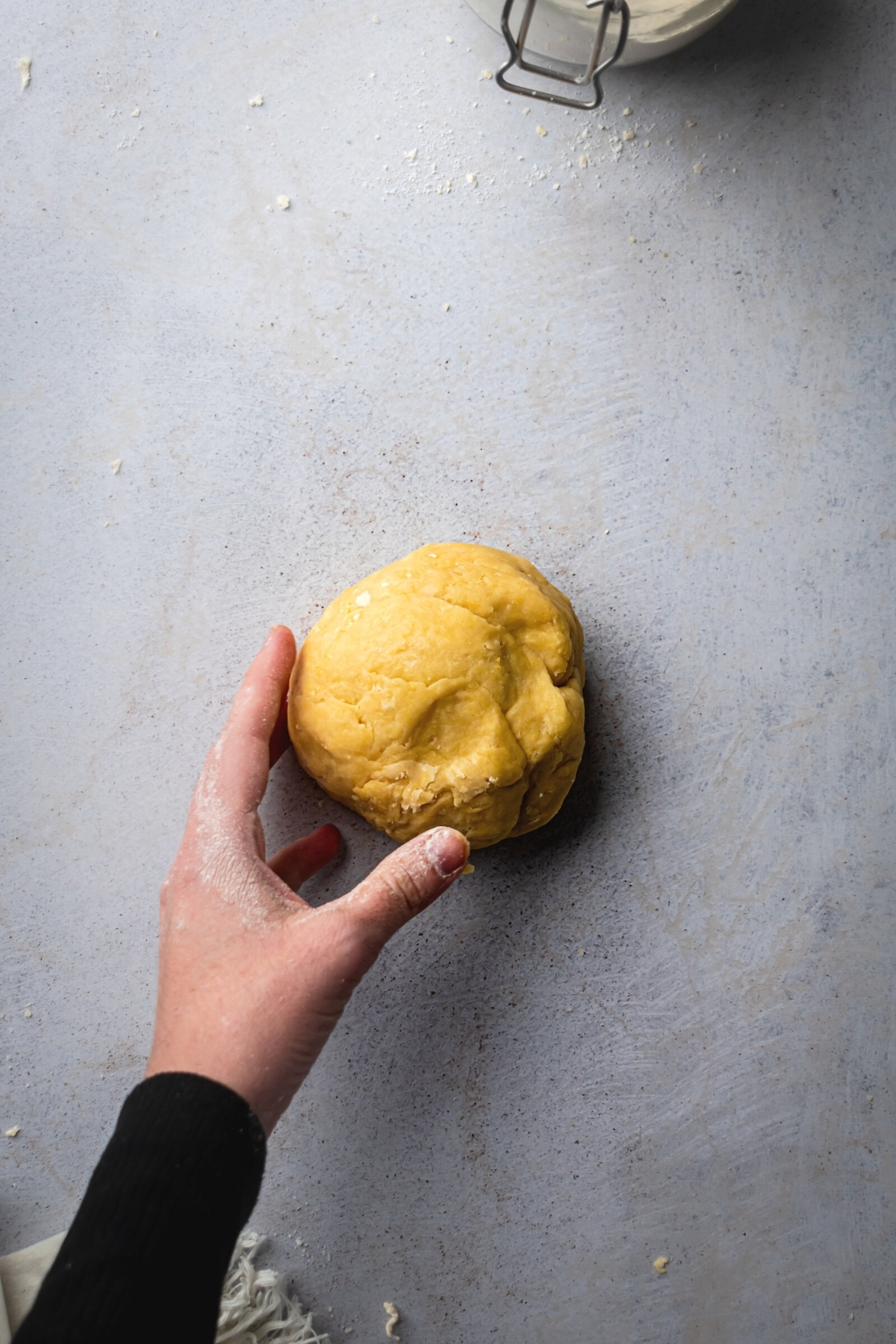 A hand holding a ball of dough on a gray counter.