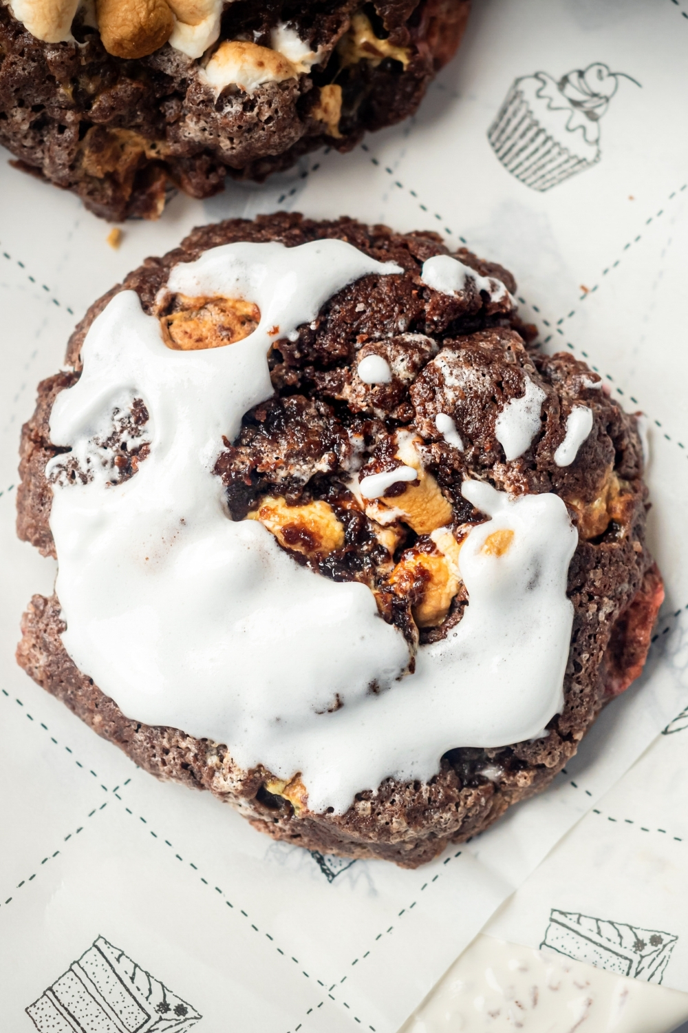 A piece of parchment paper with a chocolate marshmallow cookie with fluff on top on the parchment paper.