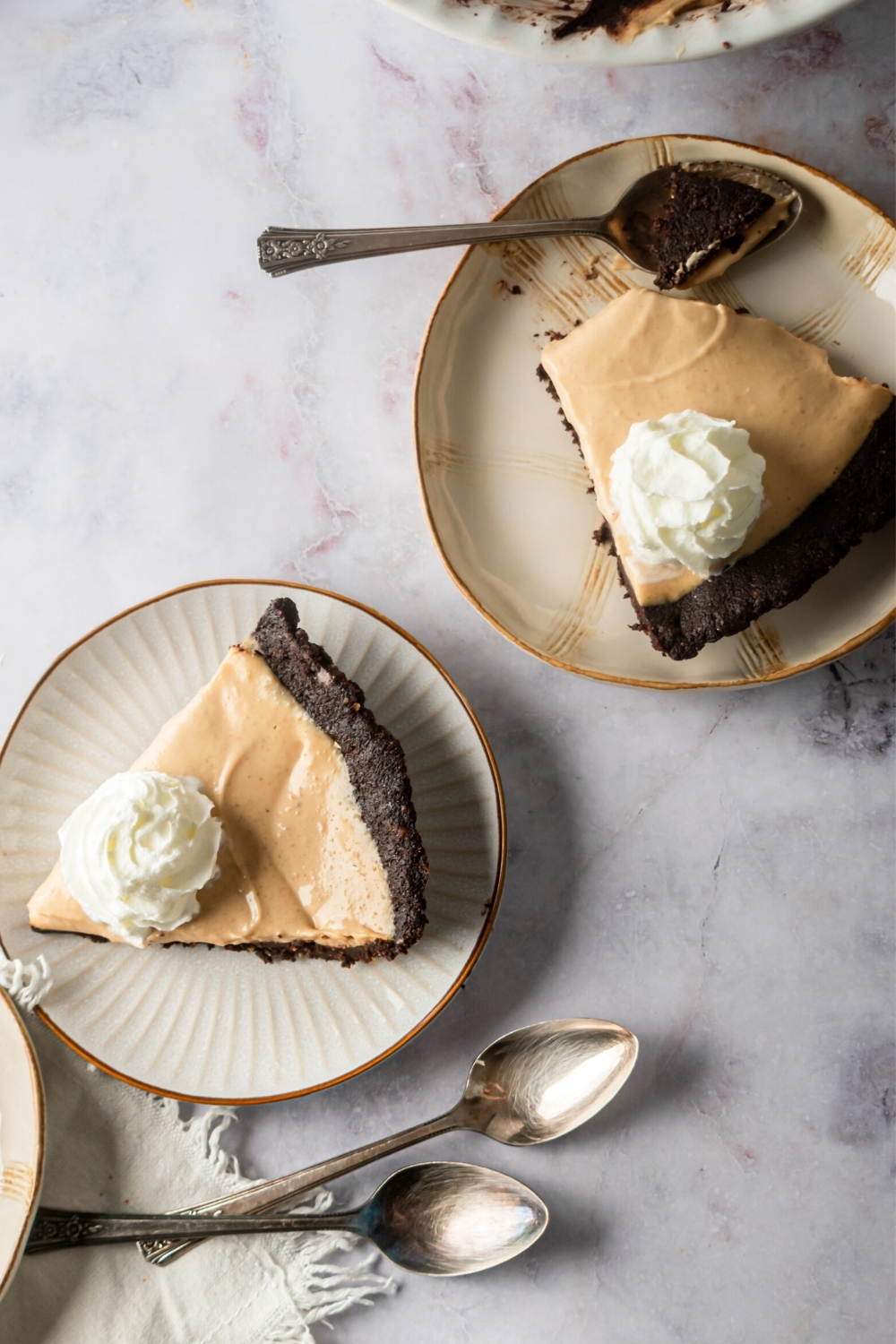 Two plates on a white counter each with a slice of chocolate peanut butter pie on it.
