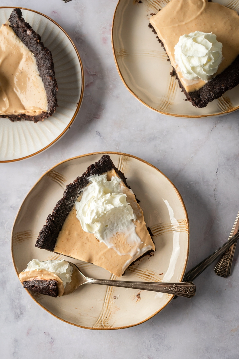 A plate with a slice of chocolate peanut butter pie on it with a piece missing from the front that is on a spoon next to the pie on the plate. Behind that is part of two more plates with part of peanut butter chocolate pie slices on it.