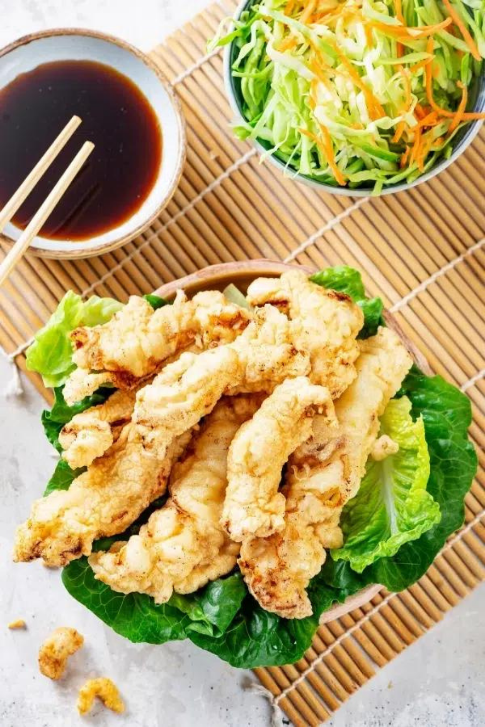 Chicken tempura on lettuce in a bowl on a straw place mat.
