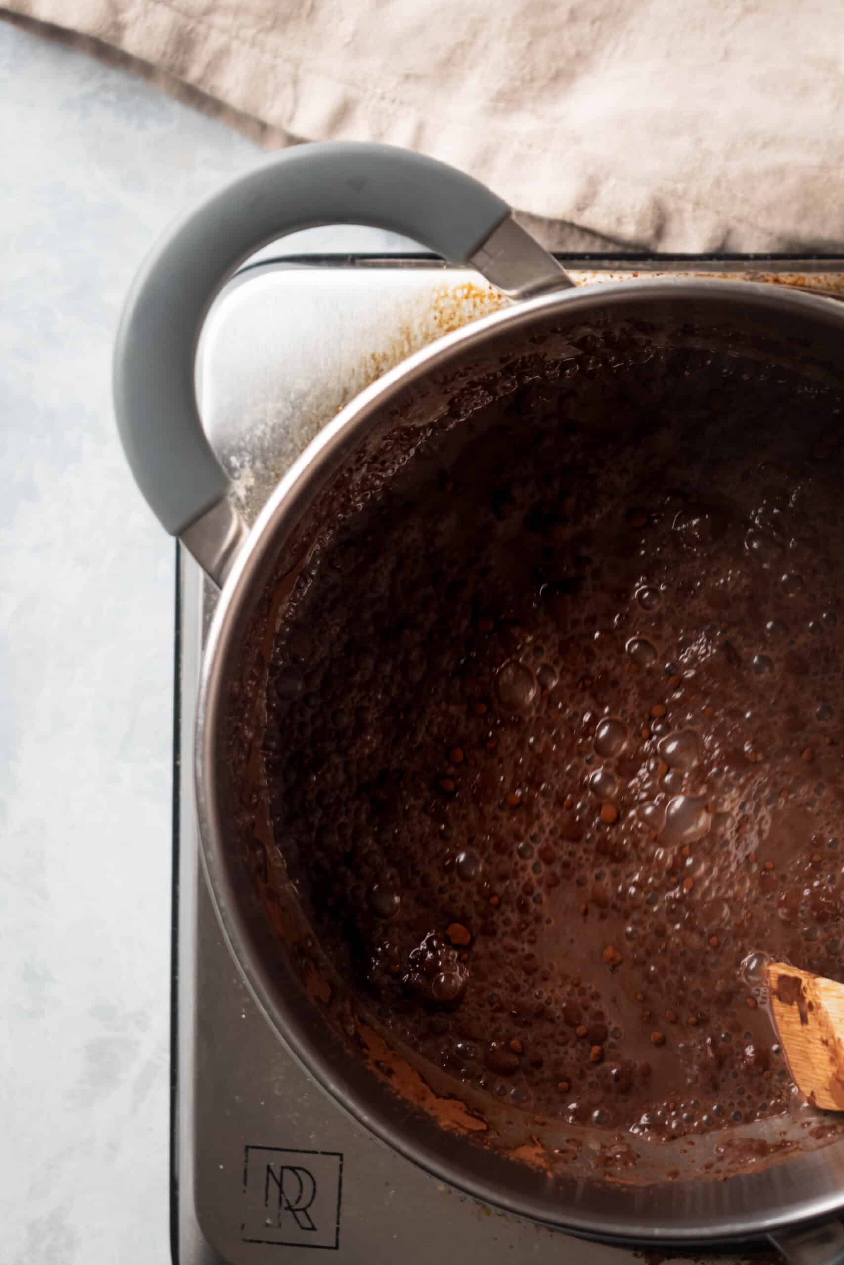 A pot on a burner filled with bubbling hot chocolate.
