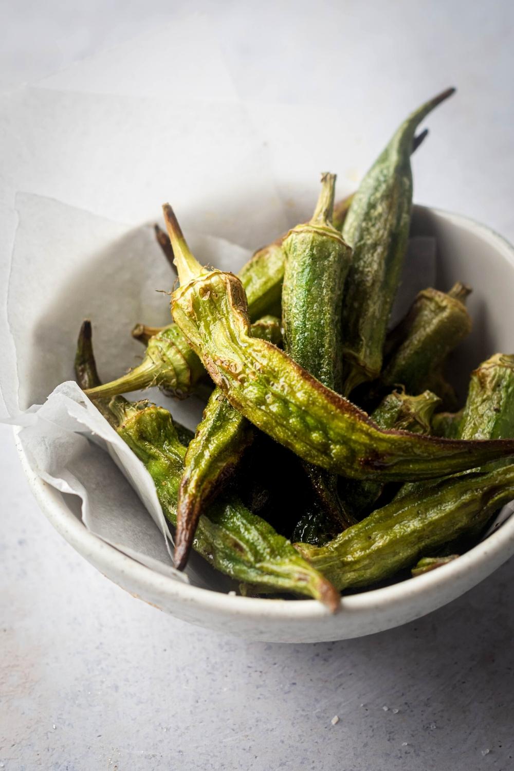 A bunch of fried okra in a white bowl lined with parchment paper.