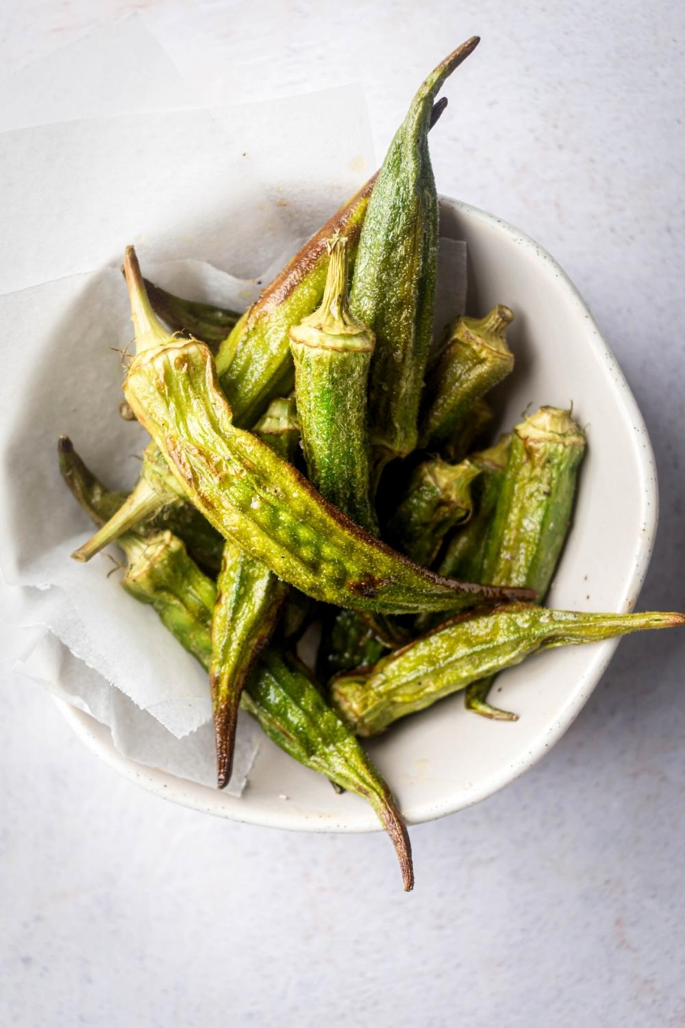 Fried okra on top of parchment paper in a white bowl.