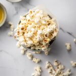 Popcorn in a tin cup on a grey counter. There is some popped popcorn around the bowl.