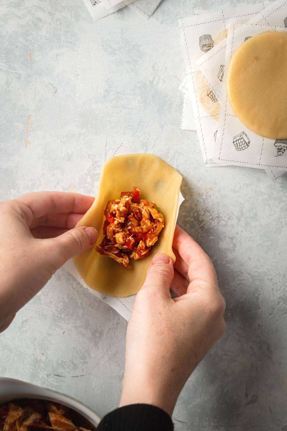 Two hands folding a empanada discs filled with chicken empanada filling.