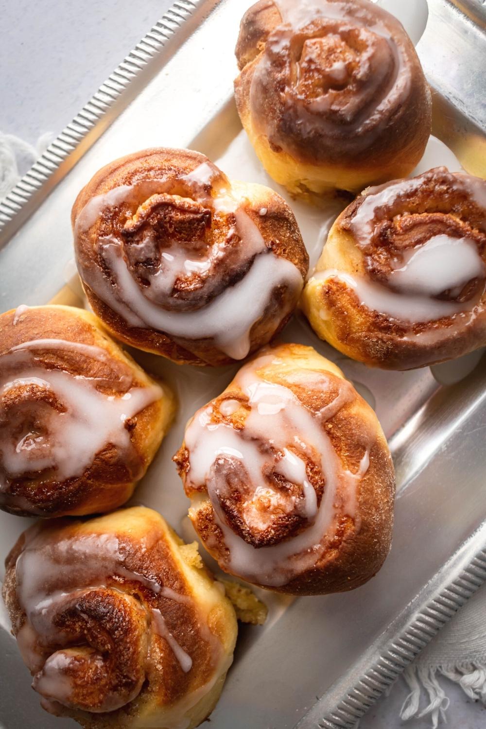 Diagonally placed silver serving dish with six cinnamon rolls on it.