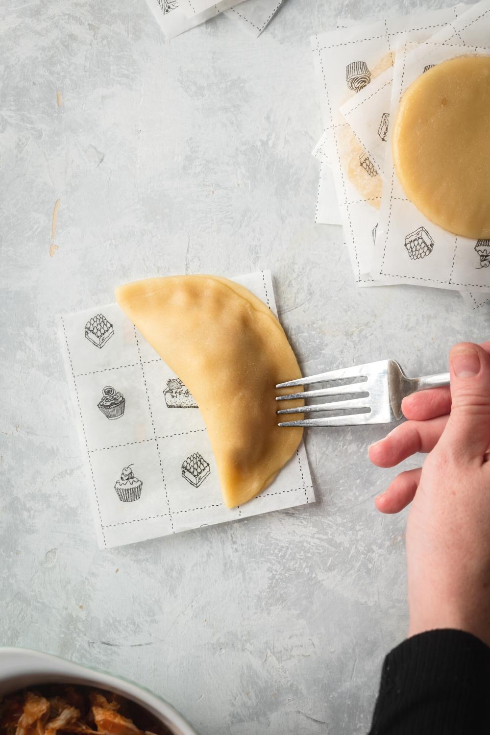 A hand pressing a fork down to seal a chicken empanada.